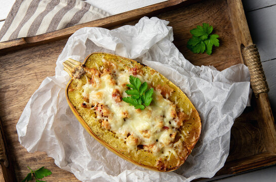 Spaghetti squash or vegetable spaghetti stuffed with minced meat and cheese, served in its shell. Homemade dish on a rustic wooden background.