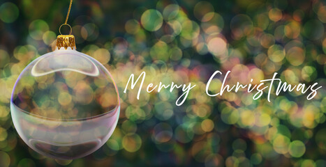 Szklana bombka choinkowa na złotej zawieszce na tle kolorowych świateł z efektem bokeh, obok napis z życzeniami: Merry Christmas © Blue Pixel