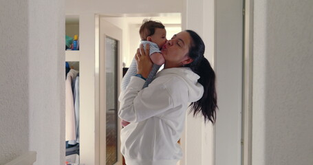 Mother lifting baby close to her face in hallway, natural light, warm and loving family moment, candid authentic lifestyle scene, nurturing and bonding