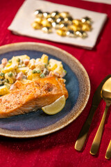 Grilled salmon fillet with russian salad and lemon slice on christmas table setting