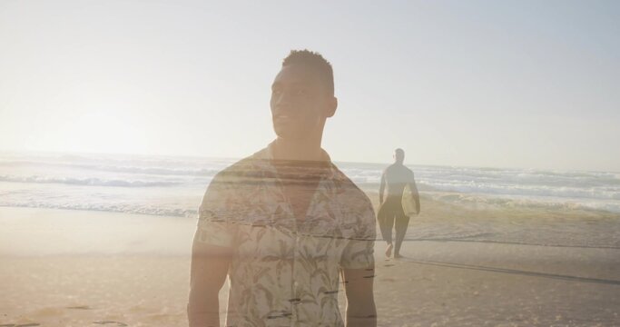 Standing man wearing palm shirt gazing at sea at sunset, surfer carrying surfboard walking shore