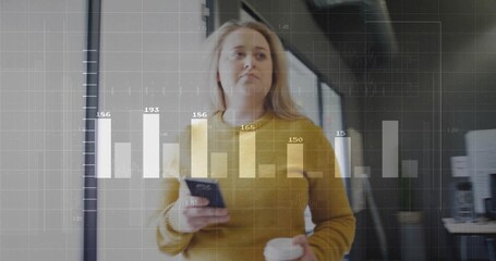 Holding coffee cup checking smartphone, mustard sweater-clad woman in office corridor, bar chart
