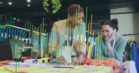 Leaning fashion designers examining sketches at studio table, with fabric swatches and sewing tools