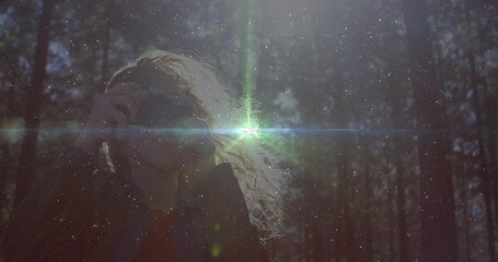 Curly haired woman taking photographs in sunlit pine forest, with lens flare and floating dust