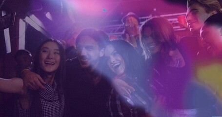 Posing seven friends on nightclub dance floor, with smartphone capturing magenta and purple lights