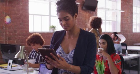 Standing South Asian woman in floral blouse and blazer using tablet in open office, with monitors