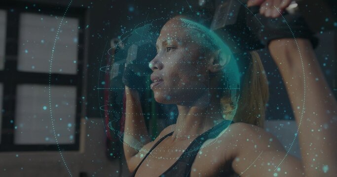 Adult African American woman pulling resistance band overhead in gym, with globe overlay and gloves