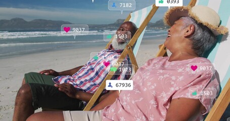 Laughing couple reclining in striped deck chairs on sandy beach, with floating social media icons