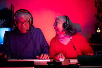 Senior couple wearing headsets and enjoying online gaming together in a neon lit room © Wosunan