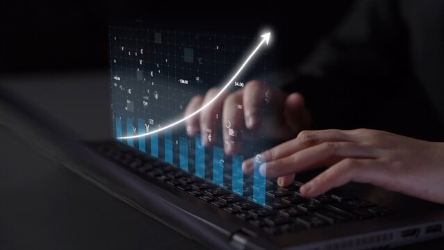 A close-up view of hands typing on a laptop, with a futuristic holographic financial graph emerging, symbolizing growth and innovation in business technology. Copula