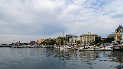 Naklejka premium Victoria inner harbour causeway glows warmly at sunset with shimmering water reflecting the colourful sky, boats gently bobbing, and the city's historic skyline creating a serene, picturesque scene.