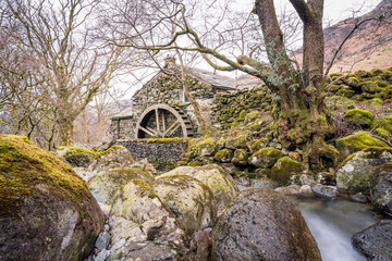Old stone mill building with wooden waterwheel and mossy stream in Lake District © CharnwoodPhoto