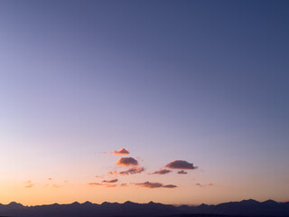 Pastel dusk sky with small clouds and a dark mountain silhouette, showing a purple-to-peach gradient at twilight.