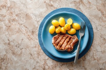 Grilled pork chop and roasted baby potatoes on a blue plate, overhead view