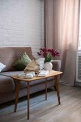 A serene living room with a comfy sofa, ceramic vase with flowers, soft cushions, and a stylish workspace for productivity and focus: keyword, notebook, earphones, bag.