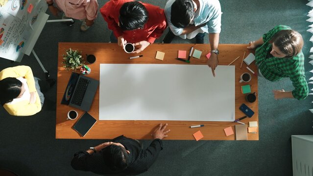 Top view of diverse business team brainstorming marketing idea while project manager standing at whiteboard. Multicultural people discuss strategy while standing around at meeting table. Convocation.