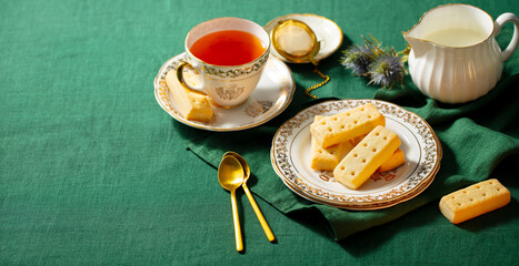 Shortbread cookies on a plate with cup of tea. Traditional Scottish dessert. Green textile background. Copy space.