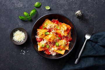 Ravioli with cheese, tomato sauce and fresh basil in black bowl. Dark background. Close up. Top...