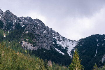  spring time sharp peaks rocky high snow covered mountains with cloudy sky landscape with green forest around