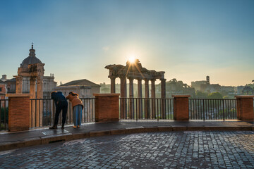 Naklejka premium Tourist couple visit Temple of Saturn at Roman forum ruins onsunrise in Rome. Italy
