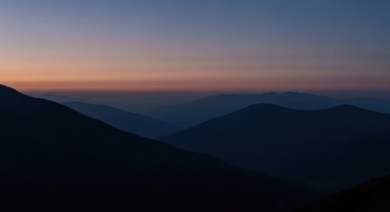 Fototapeta premium Misty mountain silhouettes at dawn. Layers of dark peaks against a pale sunrise
