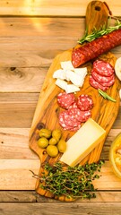 Wooden board with sliced salami, cheeses, olives, and herbs