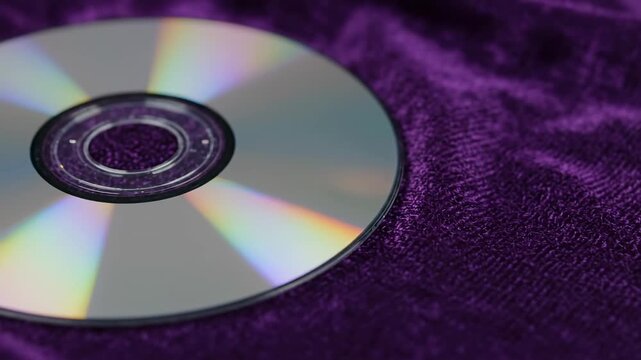 CD on Purple Velvet - A close-up shot reveals a compact disc resting on a plush purple velvet fabric. The iridescent surface of the CD is sharply in focus, contrasting with the soft texture of the