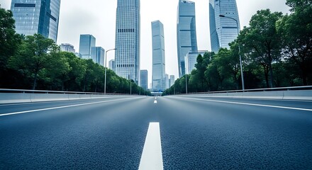 Empty asphalt road leading towards modern city skyscrapers and green trees on a cloudy day