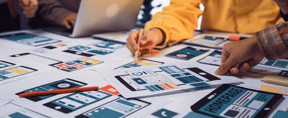 A diverse team collaborates on innovative design concepts for user-friendly mobile applications, surrounded by sketches, laptops, and brainstorming tools in a lively office. SACTR