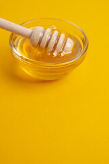 Honey drips from a wooden ladle into a glass bowl against the background of a bright kitchen.