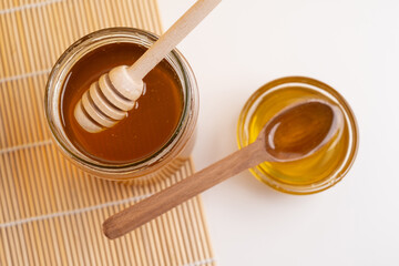 Jar of honey with wooden honey dipper on white kitchen background. Tasty honey bunker.