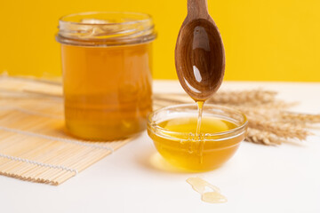 Honey drips from a wooden ladle into a glass bowl against the background of a bright kitchen.