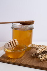 Honey drips from a wooden ladle into a glass bowl against the background of a bright kitchen.
