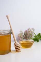 Honey drips from a wooden ladle into a glass bowl against the background of a bright kitchen.