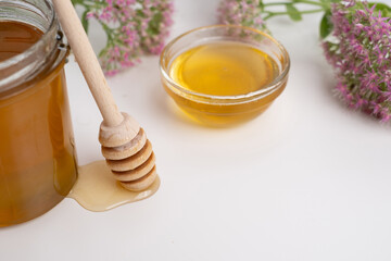 Honey drips from a wooden ladle into a glass bowl against the background of a bright kitchen.