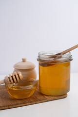 Honey drips from a wooden ladle into a glass bowl against the background of a bright kitchen.