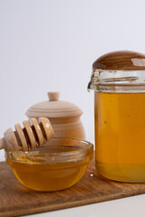 Jar of honey with wooden honey dipper on white kitchen background. Tasty honey bunker.