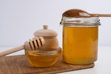 Jar of honey with wooden honey dipper on white kitchen background. Tasty honey bunker.