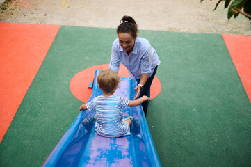 Mother Helping Child on Playground Slide Surface in Outdoor Park Setting