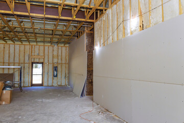 Workers are preparing interior of spacious construction site with incomplete drywall, raw structure exposed.