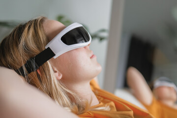 Gen Z woman unwinds  home smart eye massager?wellness tech  recovery, mindfulness and stress relief. Cozy greenery and soft light set a self-care, digital-detox mood, promoting balance, calm wellbeing