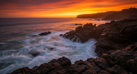 Obraz premium Dramatic Coastal Sunset: Vibrant Orange Sky, Ocean Waves Crashing on Rugged Rocks, Long Exposure Photography
