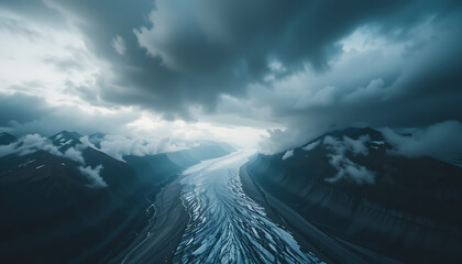 An epic aerial view captures a vast glacier winding through dramatic, cloudshrouded mountains under a stormy sky