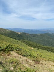 Fototapeta premium Panoramic view of green mountain slopes under a blue summer sky.