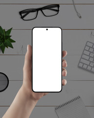 Hand holding smartphone mockup with blank screen on workspace background