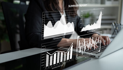 Business professional analyzes a summary report on a laptop, focusing on graphs and charts to...