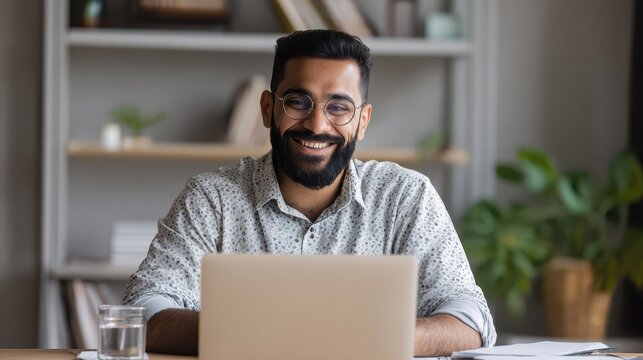 smiling bearded indian businessman working on laptop at home office young indian student using computer remote studying virtual training on video call meeting watching online webinar or seminar no lo
