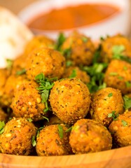 Close-up of many small, golden-brown falafel balls, piled high in a wooden bowl, garnished with fresh herbs