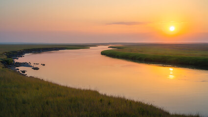 Fototapeta premium A serene river flows through a grassy landscape under a vibrant sunset sky, casting a warm orange glow on the water