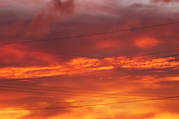 electric power lines hanging in a red burning colored sky during evening sunset